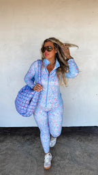 Woman in a blue floral outfit with a matching bag against a white wall.