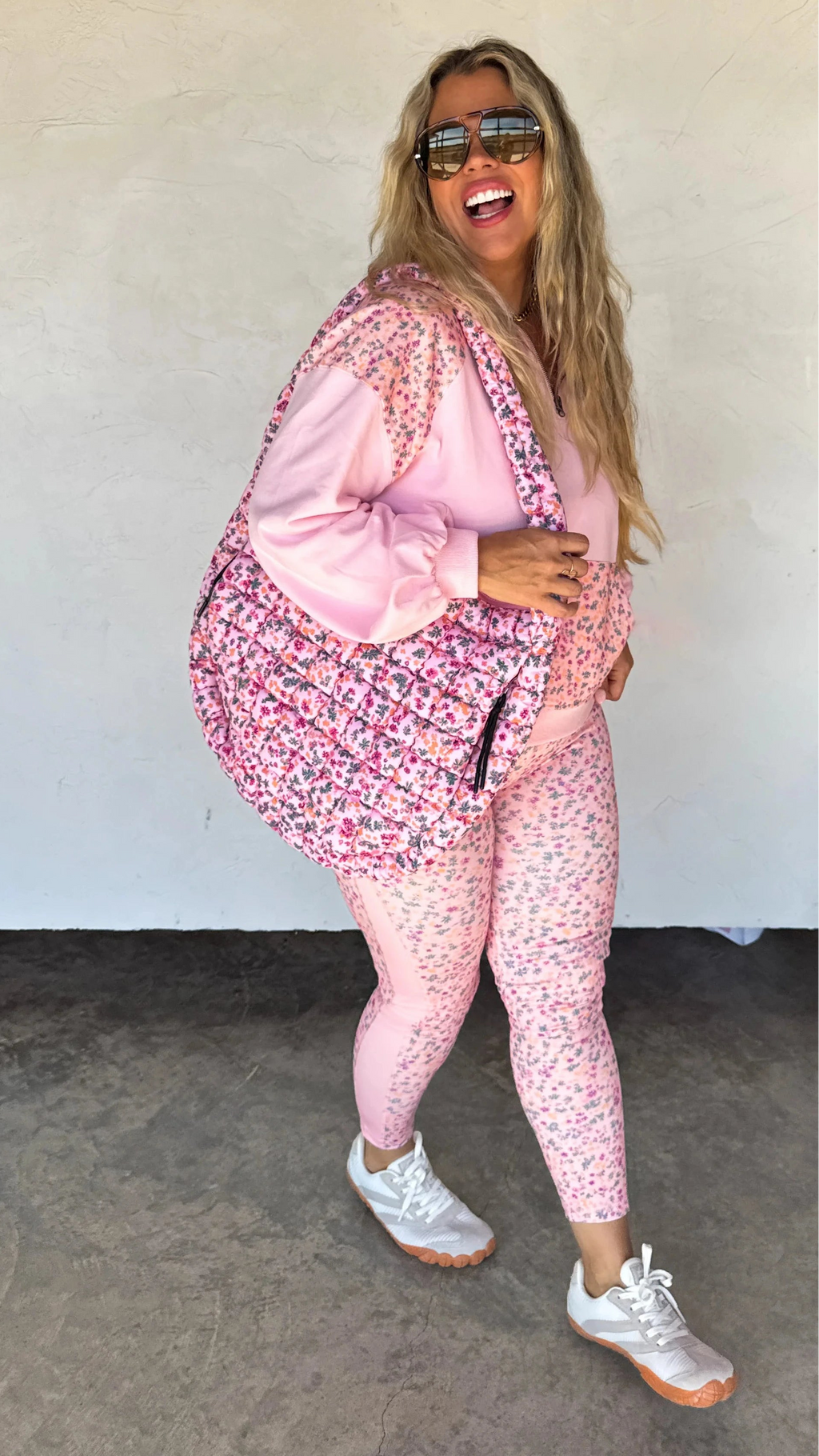 Woman wearing a pink floral outfit with sunglasses against a plain background