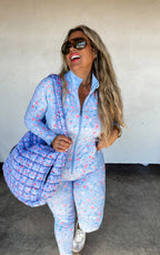 Woman wearing a blue floral outfit with a matching bag against a white wall.
